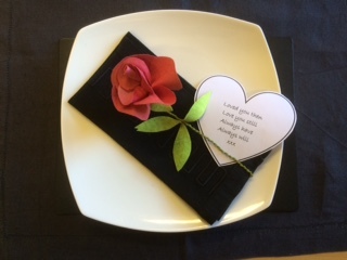 A white dinner plate and black napkin, beneath a single red rose made from Evolon Soft. There is also a heart shaped note next to the rose which reads 'Loved you then, love you still, always have, always will. xx'
