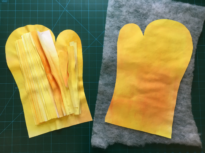 Two yellow mitten shapes, one with strips of Evolon attached to it and the other lying on top of a thin sheet of wadding