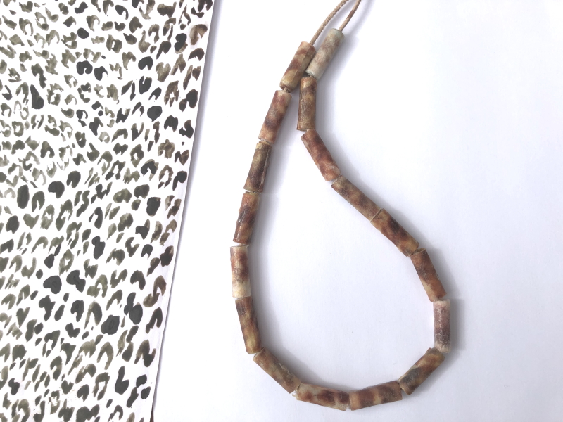 A necklace of straight mottled coloured brown beads on a beige leather strand.