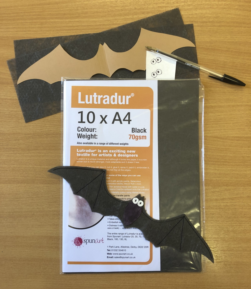 An A4 pack of Lutradur 70gsm Black, a cardboard bat template, a completed bat, a small piece of Evolon and a black biro.