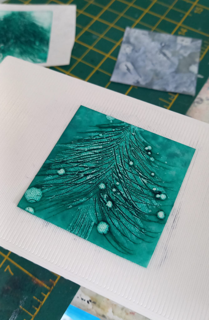 An image of a wispy Christmas tree. The branches are defined by sweeping black lines on mottled bluey-green background. There are also small blobs of lighter green dotted over the tree, perhaps representing snow or decorations.