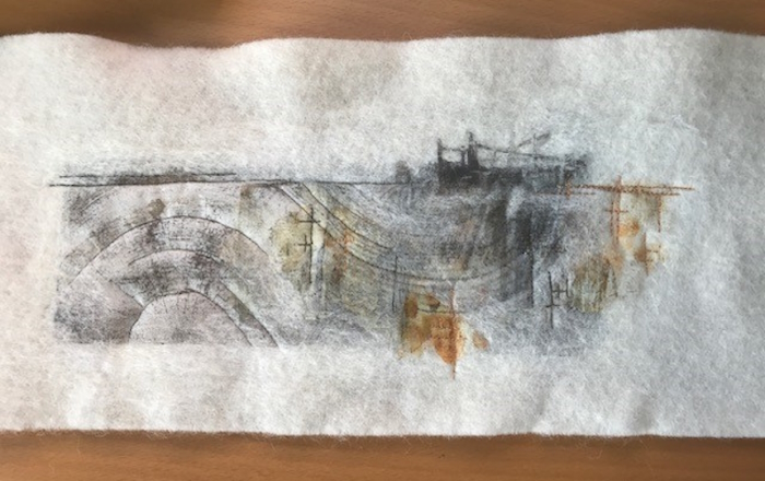 A photograph showing work in progress on a mixed media picture entitled 'The Gate'. The image is set on a natural white background and shows grey and brown abstract forms with a darker piece toward the top right, representing a gate.