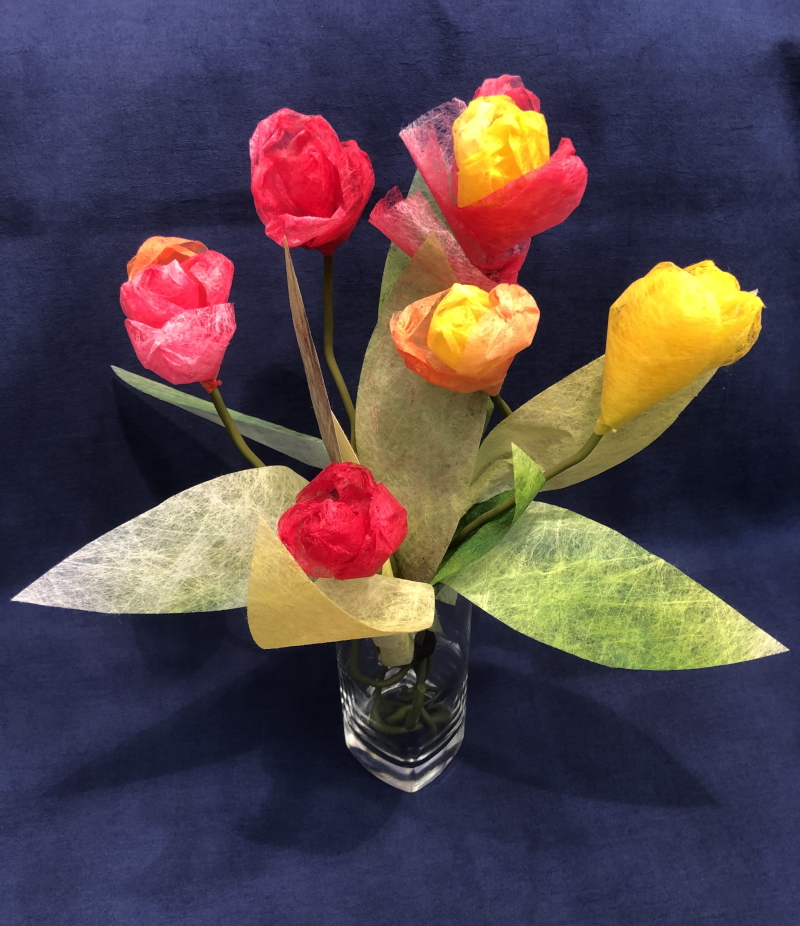 A small display of 6 completed tulips in red, yellow and a combination of yellow and red, standing in a glass with 5 green leaves.