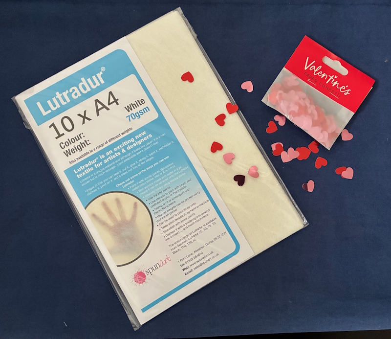 An A4 pack of Lutradur 70gsm together with a sprinkling of red and pink hearts, from a packet of Valentine's paper confetti.