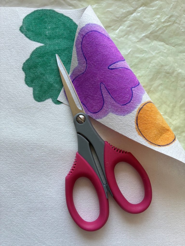 A small pair of dark red handled scissors are lying across the Evolon, which has been folded back to show the colour from the fibre pens has spread to the reverse side of the fabric.