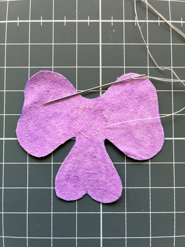 A running stitch of white cotton being sewn in a circle in the middle of the main pansy petals. 